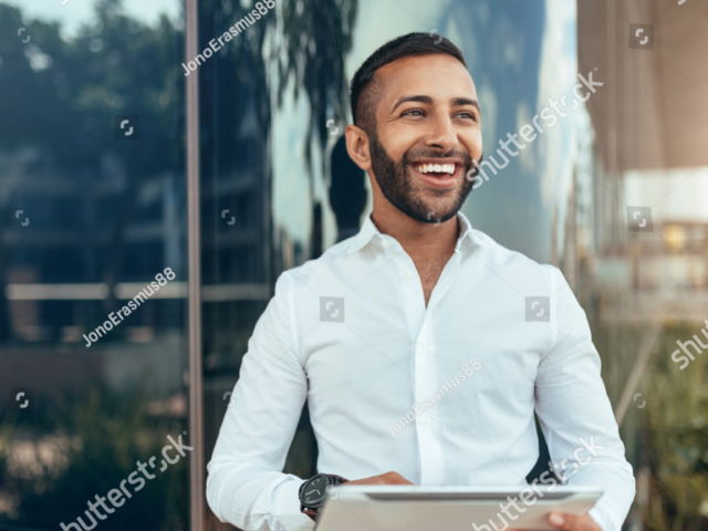 stock-photo-portrait-of-a-young-confident-smiling-indian-man-holding-a-tablet-and-looking-into-the-distance-1288131166